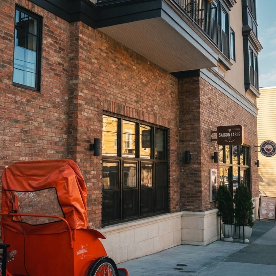 Street view of Saigon Table restaurant in a brick building, with an orange pedicab parked outside.